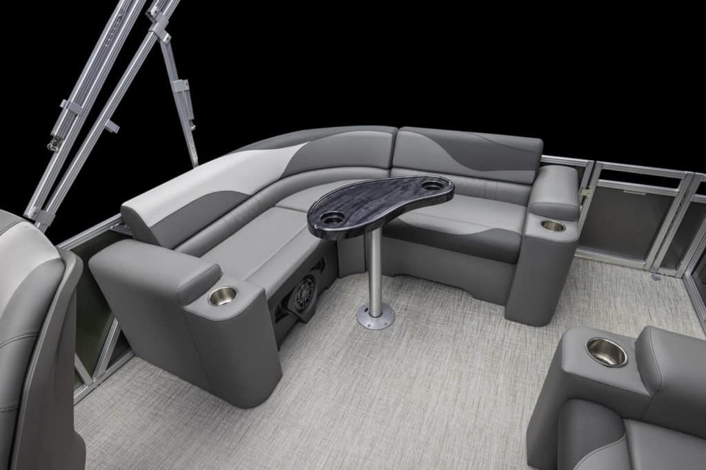 A view of a LSZ Elite's stylish seating area featuring gray cushioned seats with a U-shaped configuration and a sleek, dark oval table in the center. The flooring is a light-colored, textured material, and there are multiple cupholders integrated into the seats.