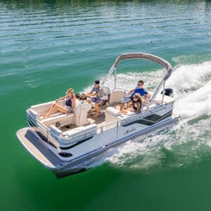 A family enjoys a sunny day on a Venture 85 Cruise gliding through calm green waters. Three people are visibly relaxed, with one steering the boat and the others lounging and enjoying the ride. A canopy provides some shade over a part of the seating area.