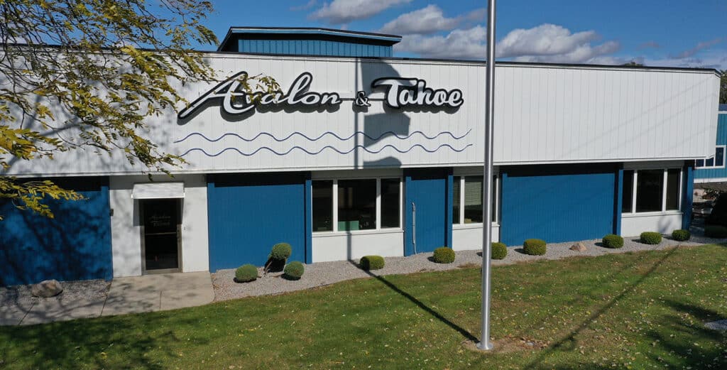 A commercial building with a white and blue exterior houses Avalon and Tahoe. The company name is displayed prominently on the front, along with wavy line designs underneath. There is a flagpole in the foreground and small bushes planted near the entrance.