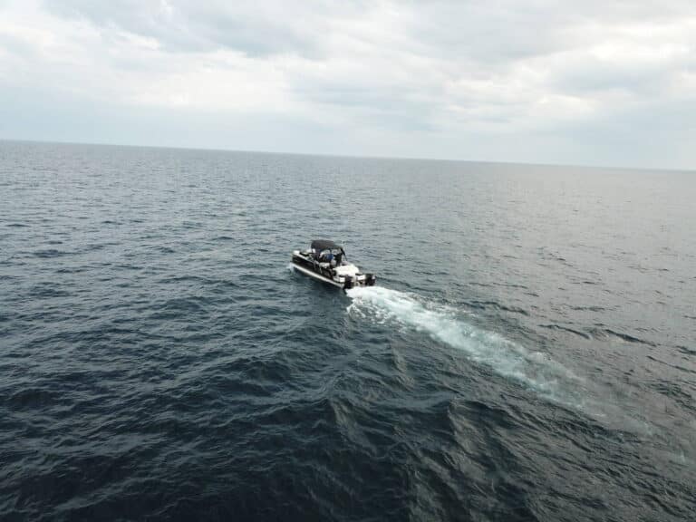 A small motorboat travels across the open ocean under a cloudy sky, leaving a trail of white water behind it.
