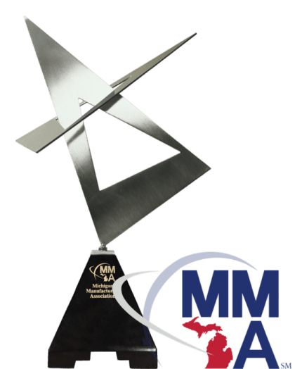 A sleek, metallic modern sculpture on a black pedestal, representing an award. The Michigan Manufacturers Association (MMA) logo featuring a graphic of Michigan's map and blue letters "MMA" is displayed at the bottom right corner of the image.