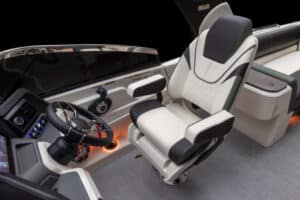 The image displays the captain's seat and steering console of a luxury boat. The seat is upholstered in white and black leather, while the console features various controls and a steering wheel. Ambient lighting is visible around the base of the seat and console.