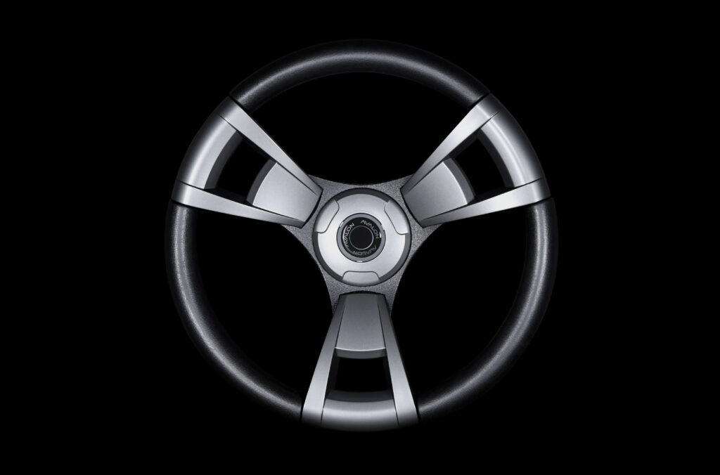 A modern, black and silver three-spoke steering wheel is centered on a black background, with metallic spokes and a circular center hub.
