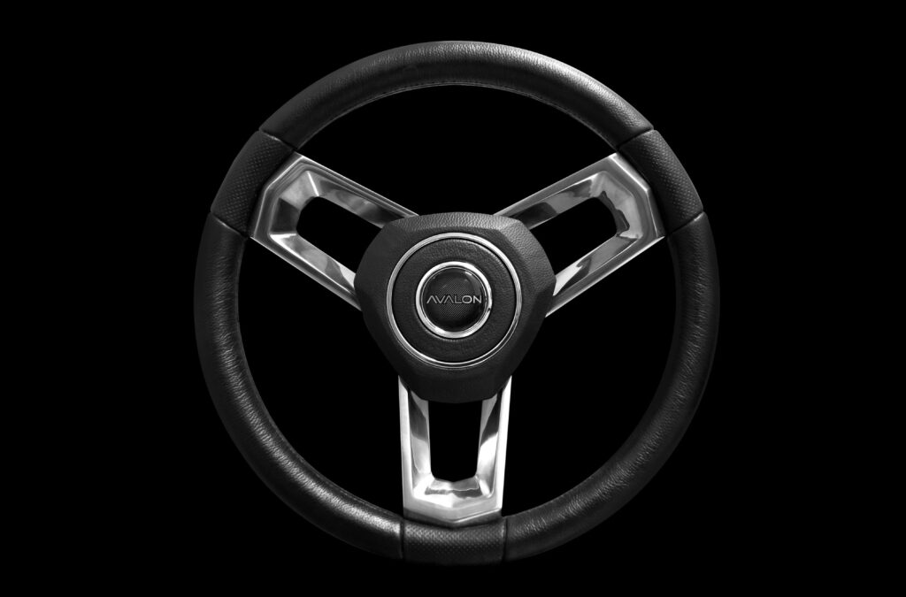 A black, three-spoke steering wheel with metallic accents and the word "AVALON" in the center, isolated on a black background.