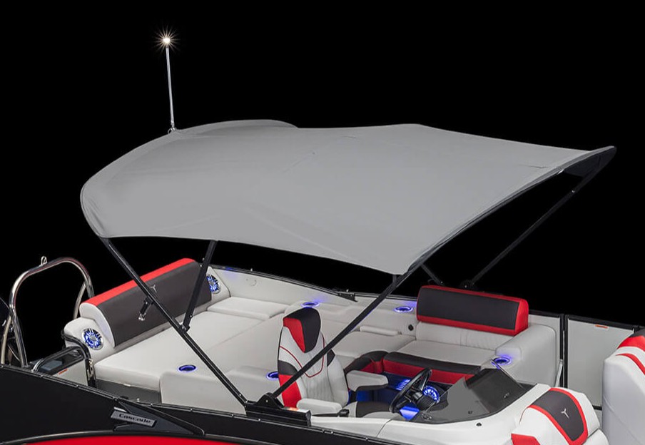 A boat with a gray bimini top canopy, featuring white and black seats with red accents, blue LED cup holders, and a small light on a pole at the rear, all set against a black background.