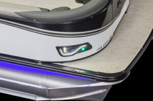 Close-up view of the corner of a boat, showing a sleek design with a green navigation light and the model name LSZ Elite displayed on the side. The boat features a stylish, metallic finish and beige flooring, with blue LED lights illuminating the lower section.
