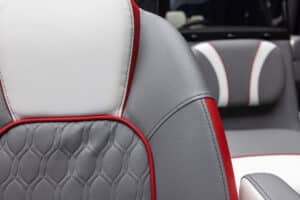 Close-up of a car seat's stylish interior design, featuring gray and white leather with red accents. The seat has a quilted pattern in the center section and smooth leather on the sides. Another seat with a similar design is visible in the background.