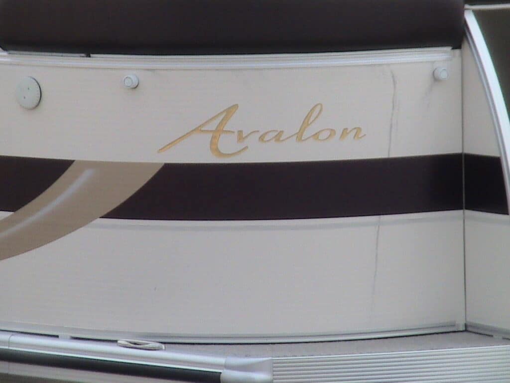 Close-up of the side of a boat, featuring the name "Avalon" written in elegant, gold script on a beige and brown striped background.