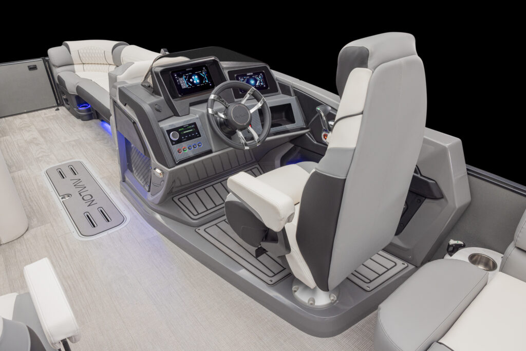 Modern boat cockpit with a steering wheel, two digital display screens, control panel, and comfortable white and gray captain’s chair. Seats and blue LED accent lighting are visible in the background.