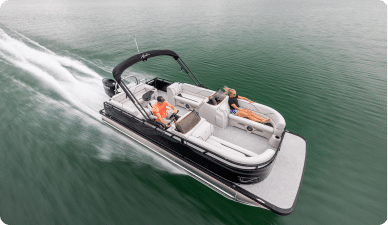 A sleek speedboat with a black canopy speeds across the water. A person is steering it while two others relax in the lounge area at the rear. The calm water parts under its hull, creating a trail of white waves that might catch the eye of anyone looking for a pontoon boat for sale.