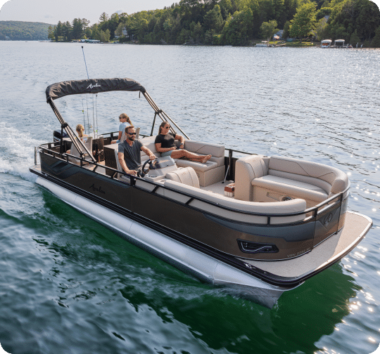A family enjoys a sunny day on their pontoon boat in a calm lake surrounded by forested hills. The boat, equipped with cushioned seating and a canopy, glides smoothly on its sturdy pontoons. The father steers while the mother and two children sit comfortably, taking in the scenic view.