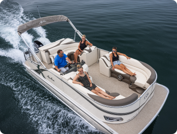 A small pontoon boat glides across a calm body of water. Four people are seated on the boat: one person is operating the vessel while the other three relax on cushioned seats. The boat leaves a gentle wake behind as it moves forward, embodying the tranquility associated with pontoons near me.
