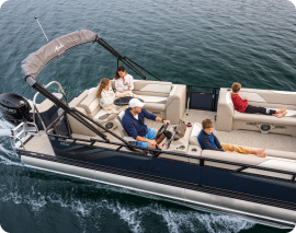 A family is enjoying a day on the water in a pontoon boat. The boat has a black canopy and beige seats. A man is at the helm steering, while an adult and three children sit on the seats, relaxing as the boat moves across the calm water. It's easy to imagine finding pontoons near me for such perfect outings.
