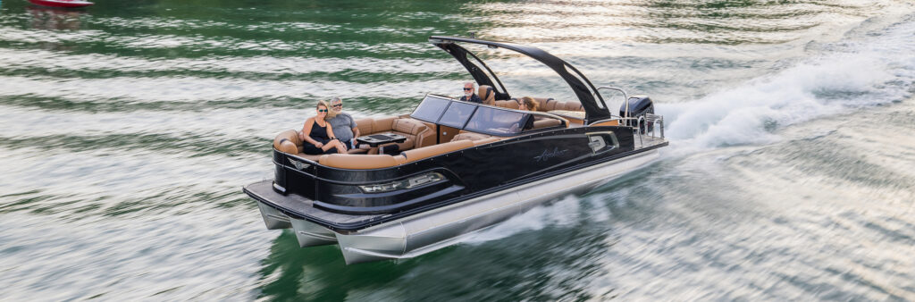A sleek black pontoon boat with brown seats speeds across the water, creating waves behind it. Onboard, three people enjoy the exhilarating ride. The water reflects the clear sky on this bright and sunny day—a perfect scene that might inspire anyone to buy pontoons for their own adventures.