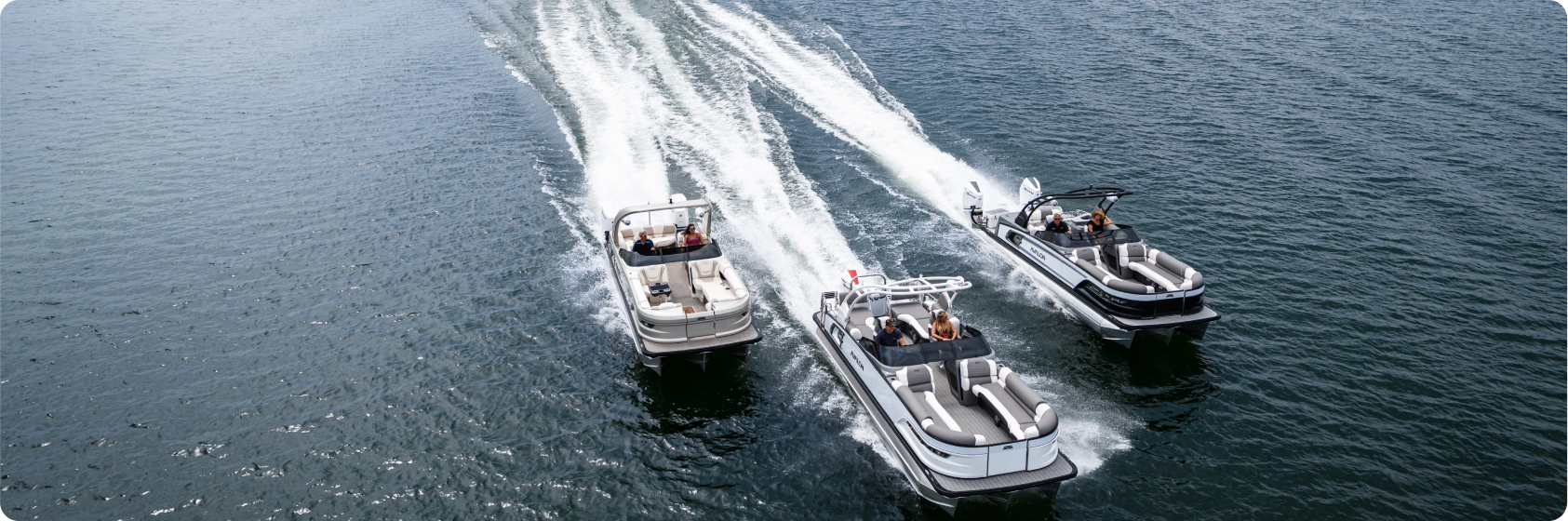 Aerial view of three motorboats cruising on a body of water, leaving white trails behind. The boats are arranged side by side with people on board each vessel, enjoying the ride under clear skies, surely a scene that would appeal to any pontoon boat dealer.