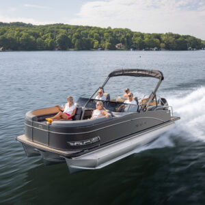 The Catalina Quad Lounger Shift Windshield glides smoothly across the tranquil lake as four passengers unwind and savor the sunlit day. Vibrant green trees border the remote shoreline beneath a sky dotted with clouds.