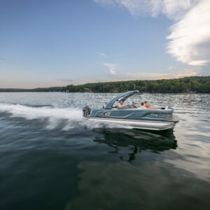 A speedboat cruises across a serene lake under a blue sky with scattered clouds. The boat creates a white wake as it moves, with lush green trees visible along the shoreline in the background.