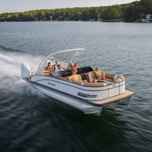 The Catalina Cruise Rear Bench Windshield glides swiftly across the lake, carrying five passengers who savor the ride under a sunny sky. The boat leaves a wake in the water with trees lining the shore in the distance.