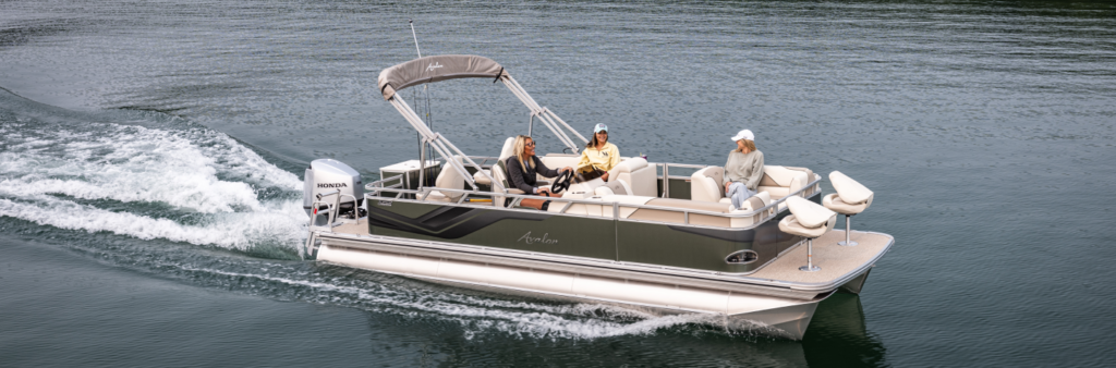 A pontoon boat with three people onboard cruises on a calm body of water. The boat is equipped with a canopy and a Honda motor. Two occupants are seated at the front, and one is at the helm. The water is gently rippling behind the boat.