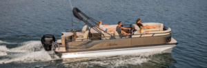 A pontoon boat with three passengers and a dog cruises on a lake. The people are seated on cushioned benches, enjoying the sunlight. The boat has a canopy frame, and its motor creates a wake in the water.