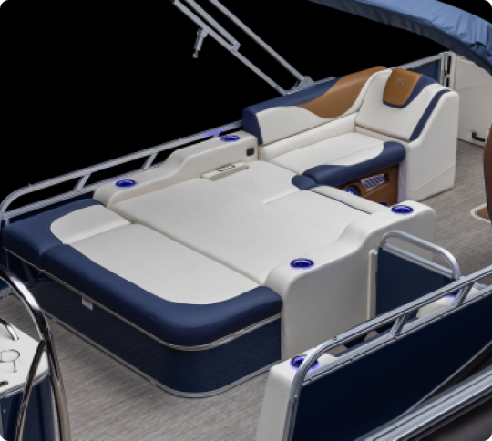The image shows the seating area on a luxury pontoon boat. The seats are upholstered in blue and white with brown accents, featuring cup holders and a sleek design. The surrounding area includes metal railings and a partial view of the floor.