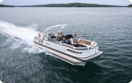 A pontoon boat glides swiftly across the lake, its four passengers reveling in the serene journey over calm, open waters. Lush green trees frame the horizon beneath a cloudy sky, making it easy to forget about everyday concerns like pontoon prices.