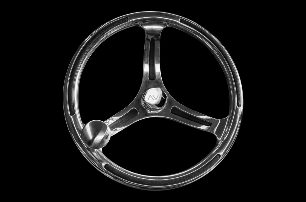 A three-spoke metallic steering wheel with a spinner knob attached to one spoke, set against a black background. The center cap displays a stylized "MV" logo.