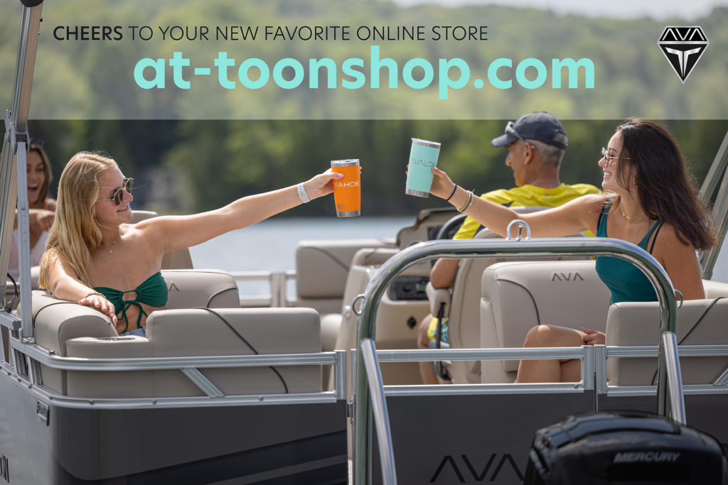 Two women in swimsuits sit on a boat, smiling and clinking drink tumblers. The background is a calm lake with trees. Text reads: "Cheers to your new favorite online store at-toonshop.com.