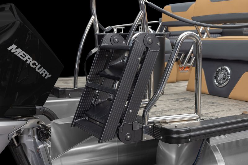 A close-up of a folded black and metal boarding ladder attached to the rear platform of a pontoon boat with tan and gray seating and a Mercury outboard motor.