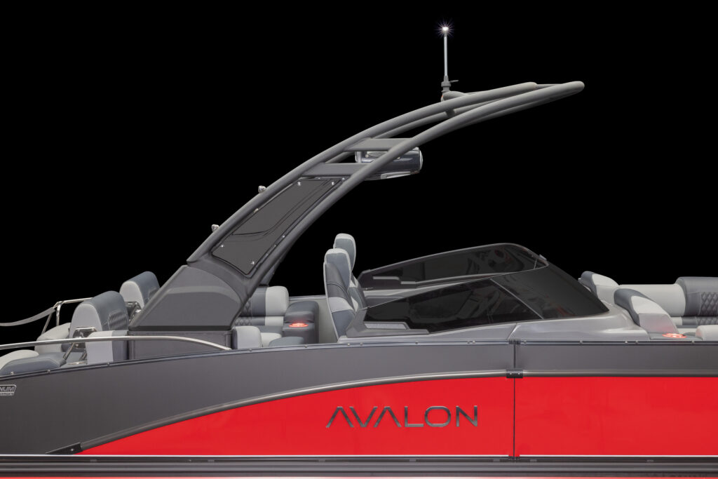 A sleek red and gray Avalon pontoon boat is shown in profile against a black background, featuring modern seating, a black windshield, and an arched tower with a navigation light on top.