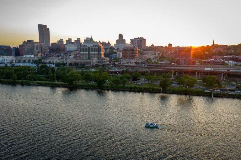 Aerial sunset view of the Avalon Patriot pontoon boat cruising on the Hudson River with the Albany skyline in the background.